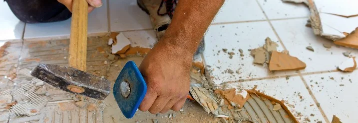 Person entfernt Fliesen mit Hammer und Meißel.